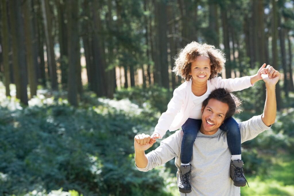 Dad with daughter on his shoulders walking in the woods in nature