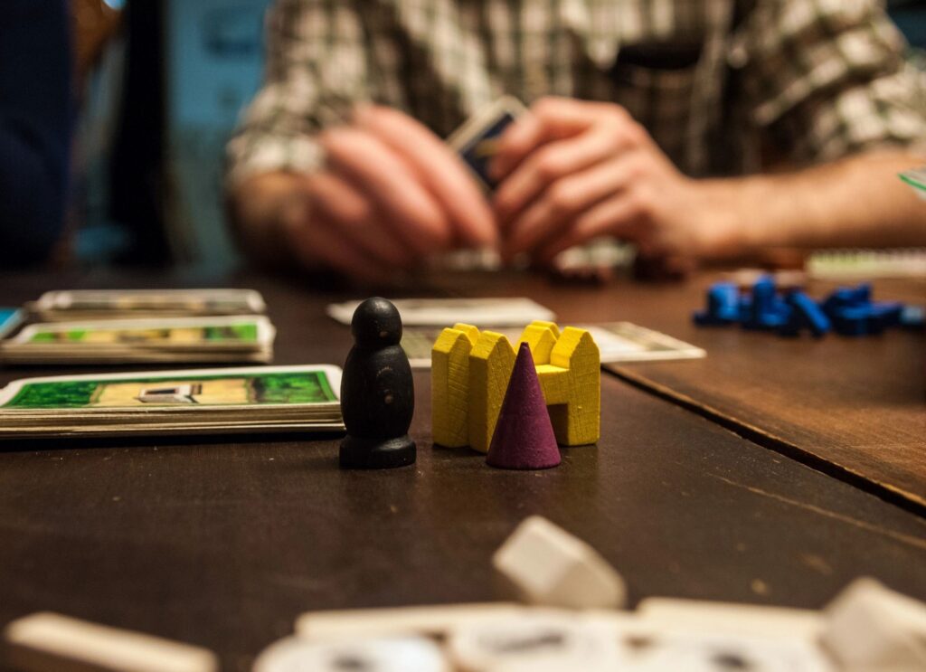 Family playing a board game seated at a table with multi-colored game pieces and decks of cards